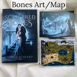 Pu&ograve; includere: Un libro intitolato "The Scattered Bones" con un'illustrazione di copertina di una coppia che si abbraccia su una scala. Accanto, due stampe artistiche: una di una coppia e un'altra di una mappa con una rosa dei venti.