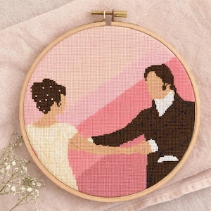 Peut inclure: Un cercle de broderie au point de croix représentant un couple dansant. Le motif utilise des nuances de rose, de marron et de crème. L'homme porte un costume marron et la femme une robe crème. Le fond présente des rayures diagonales roses.