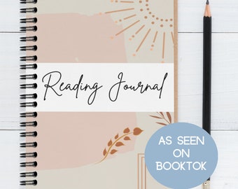 May include: A beige and pink reading journal with a spiral binding. The cover features abstract shapes, a sunburst design, and a leafy branch. The text "Reading Journal" is printed on a white label. The text "As Seen On Booktok" is printed on a blue circle.