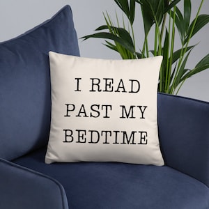 May include: A white throw pillow with black text that reads "I READ PAST MY BEDTIME". The pillow is on a blue couch.