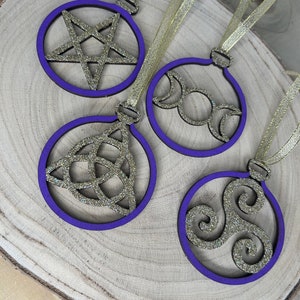 May include: Four purple and gold glitter Christmas ornaments with different symbols. The symbols are a pentagram, a triple moon, a Celtic knot, and a triskelion.