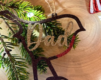 May include: A black and gold glitter Christmas ornament shaped like a robin with the word "Dad" written in gold glitter.