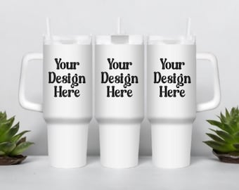 May include: Three white travel mugs with black text that reads "Your Design Here" on each mug. The mugs are on a white surface with a green succulent plant on each side.