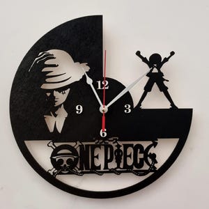 May include: A black and white circular wall clock with a red second hand. The clock features a silhouette of a character from the anime One Piece, the words 'ONE PIECE' and a skull and crossbones design.