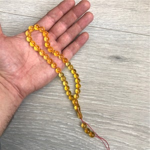 May include: A yellow amber prayer beads necklace with a red string tassel.