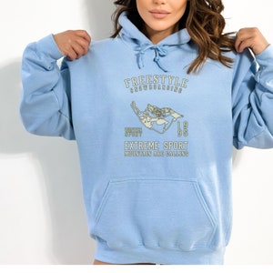 May include: Light blue hoodie with a graphic print of a snowboarder and the text "FREESTYLE SNOWBOARDING WINTER SPORT 1995 EXTREME SPORT MOUNTAIN ARE CALLING".