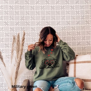 May include: A green sweatshirt with a black bulldog wearing red glasses and surrounded by red hearts. The sweatshirt is on a person wearing blue jeans.