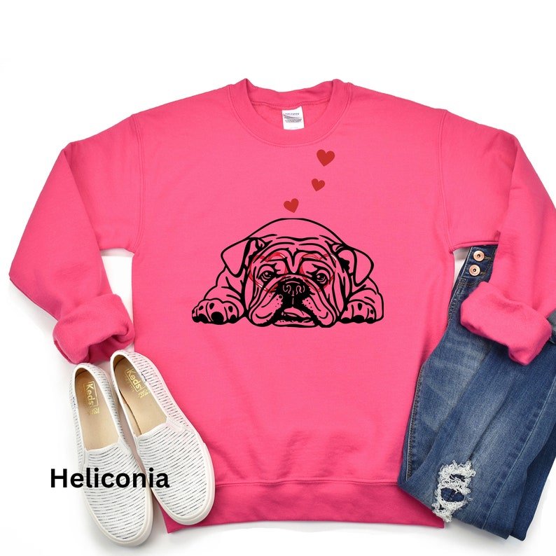 May include: A pink sweatshirt with a black bulldog illustration wearing heart-shaped glasses.  There are four red hearts above the bulldog.