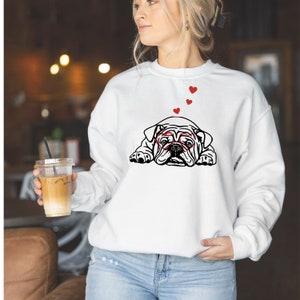May include: White sweatshirt with a black and white illustration of a bulldog wearing heart-shaped glasses.  Three red hearts are floating above the bulldog.