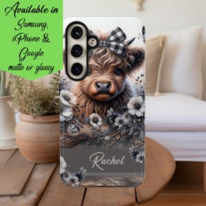 May include: A phone case featuring a brown Highland cow with a black and white checkered bow, surrounded by grayscale floral accents. The name "Rachel" is displayed at the bottom. The case is available for Samsung, iPhone, and Google phones.