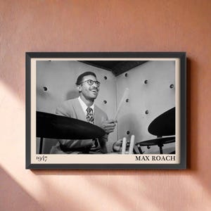 Può includere: Stampa incorniciata in bianco e nero con un uomo sorridente che suona la batteria. La stampa include il testo "1947" e "MAX ROACH". L'uomo indossa occhiali e una cravatta.