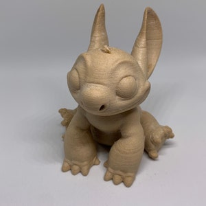 May include: A tan-colored figurine of a cartoon character with large ears, large eyes, and a wide nose. The figurine is in a seated position with its arms and legs extended. The character has a friendly expression.