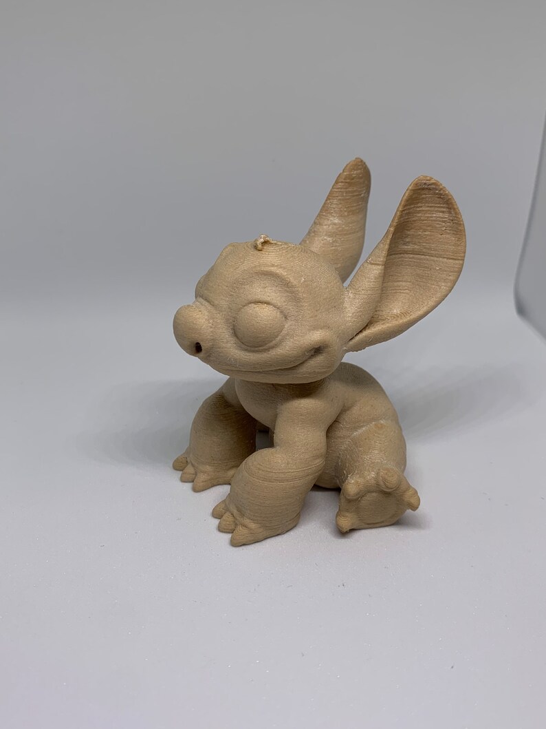 May include: A tan-colored figurine of a cartoon character with large ears, a small nose, and a smiling expression. The figurine is in a seated position with its arms and legs visible. The character's features are detailed, and the overall design is smooth.