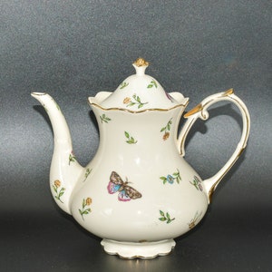 May include: A white porcelain teapot with a gold trim and floral design. The teapot has a lid with a gold knob and a handle with a gold accent. The teapot is decorated with butterflies and flowers.