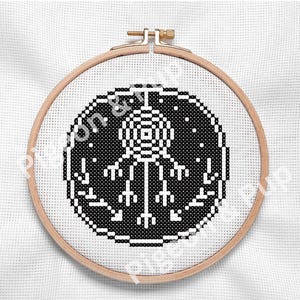 May include: A circular wooden embroidery hoop containing a cross-stitch pattern on white Aida fabric. The design features a black circular border enclosing a white pixelated dreamcatcher motif with hanging feathers and small star-like dots.