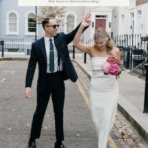 May include: A couple celebrates on a cobblestone street. The person on the left wears a dark suit, sunglasses, and a green tie. The person on the right wears a white strapless dress and carries a bouquet of pink flowers. Text reads: "I was perfect & exactly how I'd imagined."