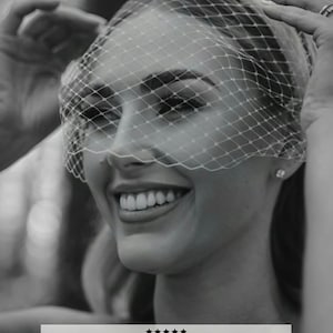 May include: A black and white image of a bride wearing a birdcage veil. The veil is made of a delicate, diamond-patterned netting. The bride is smiling, and the veil is attached to a hair band. The image includes text.