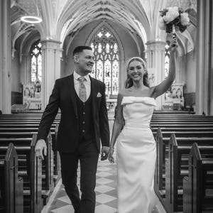 May include: A grayscale image of a wedding couple walking down the aisle of a church. The bride wears a white, strapless dress and holds a bouquet. The groom wears a dark suit. The image includes the text "Bride Chloe by @infiniteimages_".