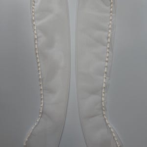 May include: A pair of long, sheer white gloves made of a translucent mesh fabric. Each glove features a vertical row of small, round, white faux pearl buttons running along the outer edge from the wrist to the top opening of the garment.