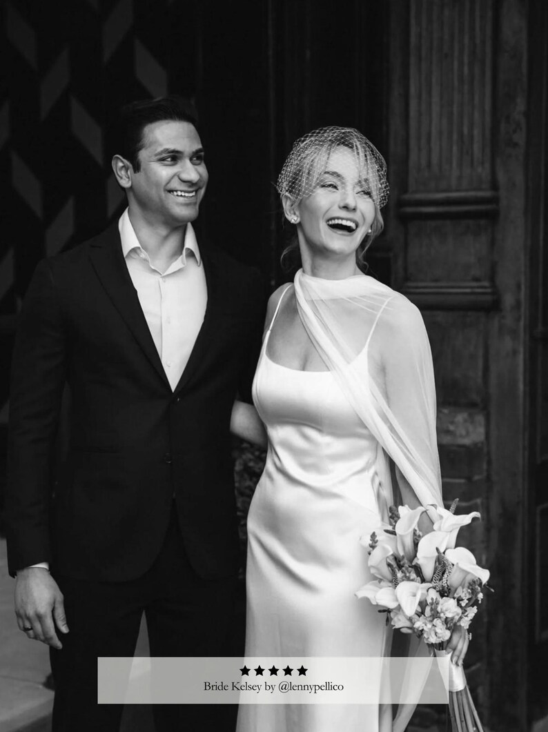 May include: Black and white photo of a smiling couple on their wedding day. The bride wears a white satin gown and veil, holding a bouquet. The groom is in a black suit. Text at the bottom reads "Bride Kelsey by @lennypellico".