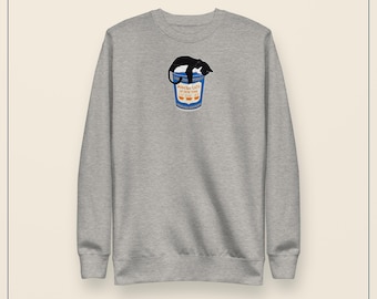 May include: A heather gray crewneck sweatshirt featuring a central graphic of a black cat resting on top of a blue and white cup. The cup displays the text "POPCORN CATS OF NEW YORK" in orange lettering above three small orange bowl icons.
