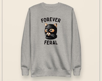May include: A heather gray crewneck sweatshirt featuring a graphic of a cat wearing a black balaclava. The text "FOREVER" is printed in black above the cat, and the text "FERAL" is printed in black below the cat, centered on the chest.