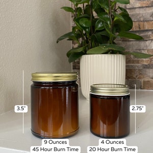 May include: Two amber glass candle jars with gold lids. The larger jar is 3.5 inches tall and holds 9 ounces of candle wax. The smaller jar is 2.75 inches tall and holds 4 ounces of candle wax. The larger jar has a burn time of 45 hours and the smaller jar has a burn time of 20 hours.