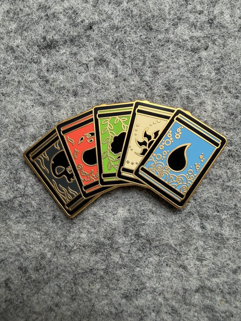 May include: Five enamel pins with gold borders, each featuring a different design: a skull, a flame, leaves, a sun, and water droplets. The pins are in a row, with a gray background.