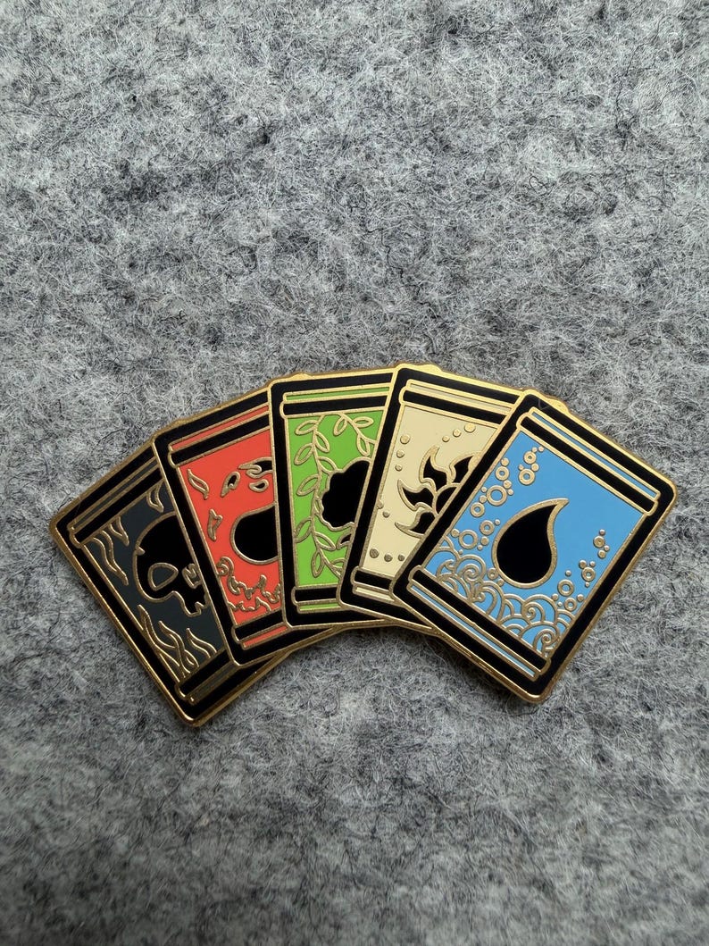 May include: Five enamel pins with gold trim, each featuring a different design. The pins are arranged in a fan shape, showcasing a skull, a stylized flame, a leafy design, a floral pattern, and water droplets. The pins have black, red, green, cream, and blue backgrounds.