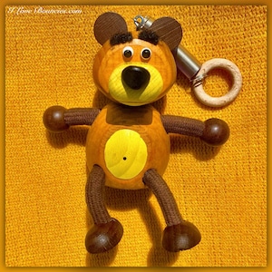 May include: A wooden bear toy with brown fur, black eyes, and a yellow belly. The bear is attached to a wooden ring with a spring.