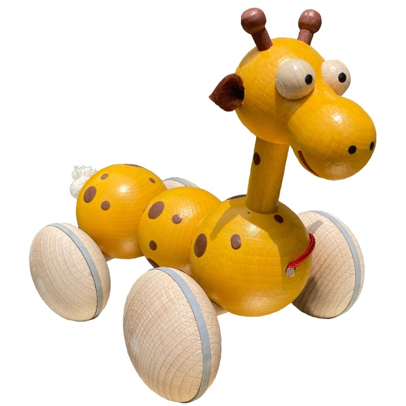 Pu&ograve; includere: Un giocattolo di giraffa di legno giallo con macchie marroni e una corda di traino rossa. La girafa ha grandi occhi bianchi e un sorriso amichevole. Il giocattolo ha quattro ruote di legno.