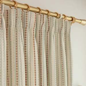 May include: Close-up of a set of white and blue striped curtains with brown accents hanging from a gold curtain rod.