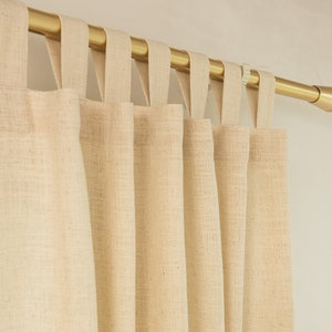 May include: Beige linen curtains with a gold curtain pole. The curtains have a simple design with a loop top and are hung in a window.
