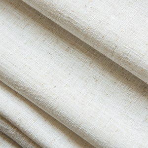 May include: Close-up of a white linen fabric with a textured weave. The fabric is folded in layers, creating a soft and natural look.