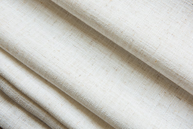 May include: Close-up of a white linen fabric with a textured weave. The fabric is folded in layers, creating a soft and natural look.
