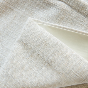 May include: Close-up of a white linen fabric with a textured weave. The fabric is folded over itself, creating a triangular shape.