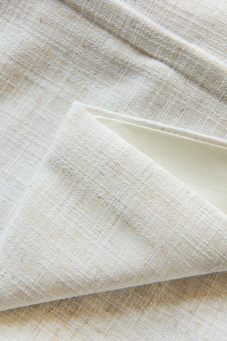 May include: Close-up of a white linen fabric with a textured weave. The fabric is folded over itself, creating a triangular shape.