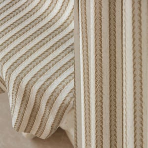 May include: Close-up of two fabric swatches with a striped pattern. The fabric on the left has diagonal stripes, while the fabric on the right has vertical stripes. Both fabrics are a light beige color with brown stripes.