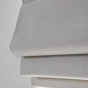 Puede incluir: Primer plano de una estor romano de color gris claro con tejido texturizado. El estor est&aacute; parcialmente subido, mostrando las capas de tejido.