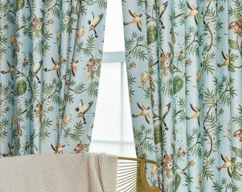 May include: A pair of light blue curtains with a floral pattern featuring birds and leaves. The curtains are hanging in a window with a gold chair and a white throw blanket in the foreground.