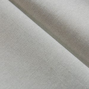 Puede incluir: Primer plano de una tela lisa de color gris claro con una textura sutil. La tela est&aacute; doblada por la mitad, creando un drapeado suave y fluido.