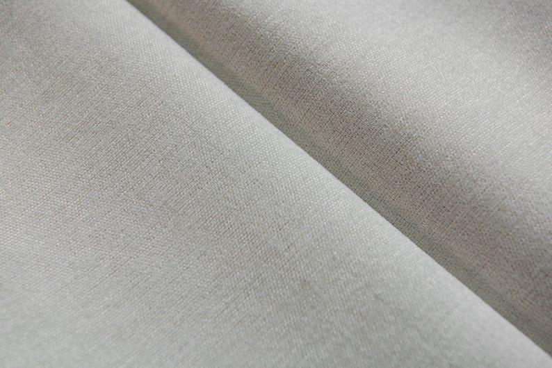Puede incluir: Primer plano de una tela lisa de color gris claro con una textura sutil. La tela est&aacute; doblada por la mitad, creando un drapeado suave y fluido.
