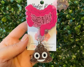 May include: Pink glitter poop emoji badge reel with a pink glitter intestine charm. The badge reel has a silver clip and a silver swivel hook. The charm is attached to the swivel hook. The badge reel is on a white card with the text "Pink Pig Vinyl" and "shop.Etsy.com/PigVinyl".