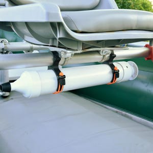 May include: A close-up of a boat interior with a gray seat and a white cylindrical object attached to the frame. The object is secured with black and orange straps. An orange container is also attached.