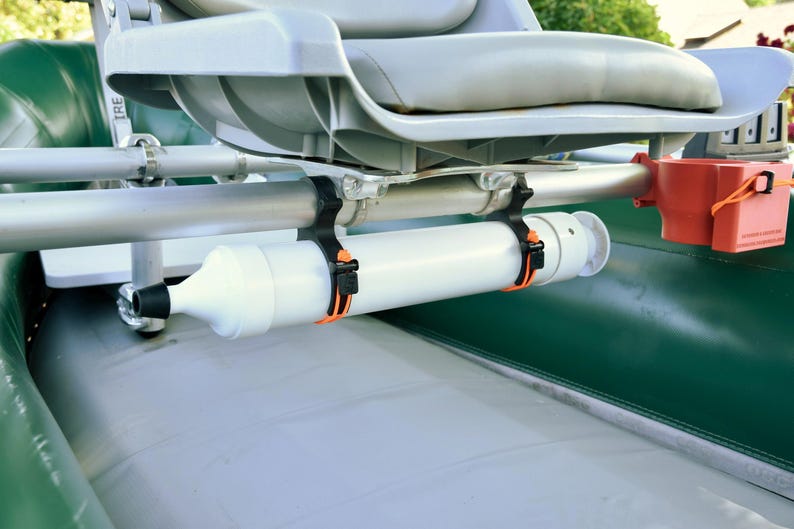 May include: A close-up of a boat interior with a gray seat and a white cylindrical object attached to the frame. The object is secured with black and orange straps. An orange container is also attached.