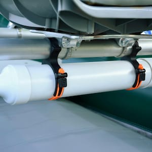May include: A white cylindrical accessory with a black nozzle and a white cap, mounted on a boat. The accessory is secured with black and orange straps to a metal bar. The boat has a green and gray color scheme.