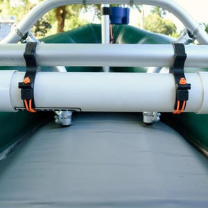 May include: A white cylindrical water pump is mounted on a green inflatable raft. The pump is secured with black straps and orange accents. The raft has a gray interior and a silver metal frame.