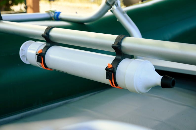 May include: A white cylindrical boat accessory with a black nozzle and orange straps, attached to a silver bar with black brackets. The accessory is mounted on a green surface, likely a boat.
