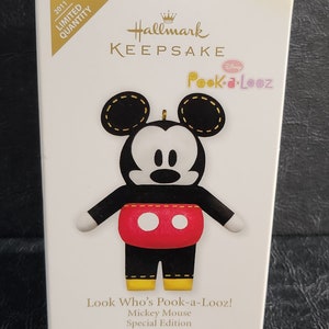 May include: A Hallmark Keepsake Christmas tree ornament featuring Mickey Mouse from the Disney Pook-a-Looz collection. The ornament is a special edition from 2011. The box is white with gold lettering and a cartoon image of Mickey Mouse.