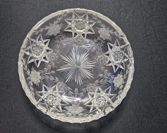 Può includere: Ciotola di vetro trasparente con disegni incisi di stelle e fiori. La ciotola presenta un motivo centrale a stella e circondato da motivi dettagliati di stelle e fiori. Il bordo ha un bordo smerlato.